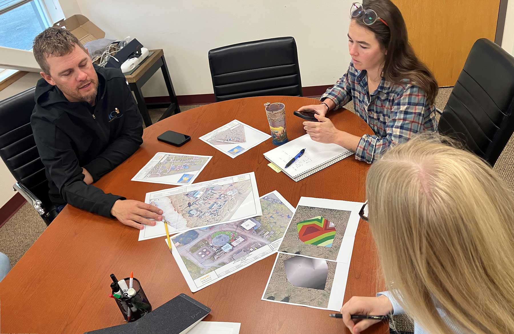 three people sitting at a table looking at maps