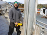 Jacob Blowers, Captain of the Free Reign, works on the vessel to prepare it for the season. May, 2024. Man with drill conducting maintenance on the Free Reign vessel. Blue sky.